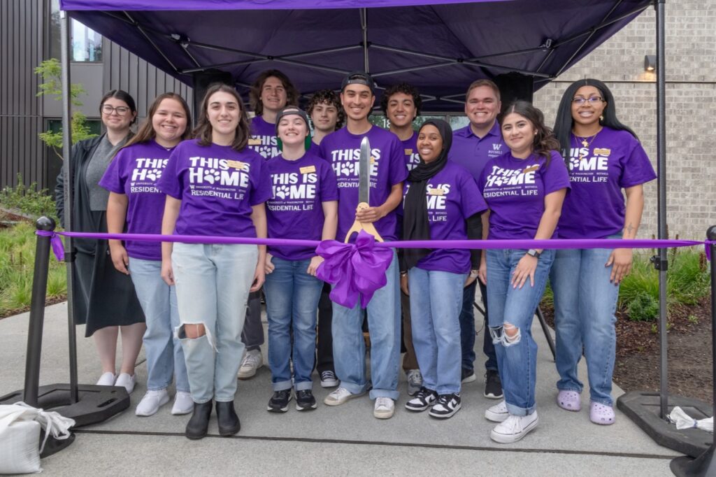 A group of people in matching purple shirts stand behind a purple ribbon.