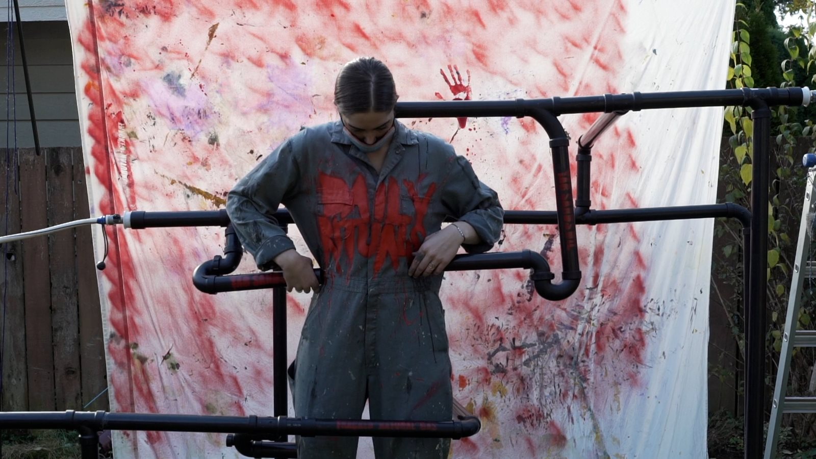 still from Broken Promises showing a person in coveralls standing on scaffolding in front of a painted background