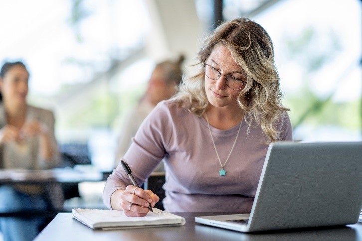 An image of a woman sitting at a table and writing on a notepad