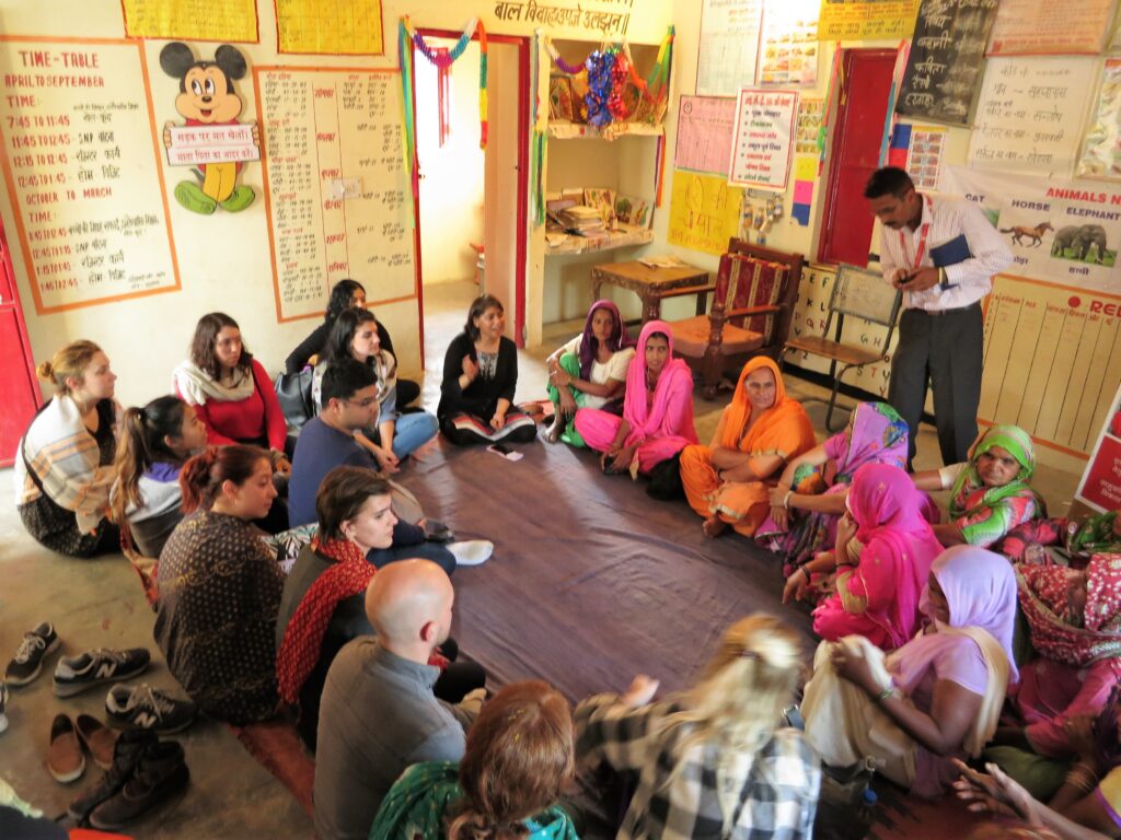 Group of people - village women in India and students from UW Bothell - sitting in a circle on the floor of a child education center classroom
