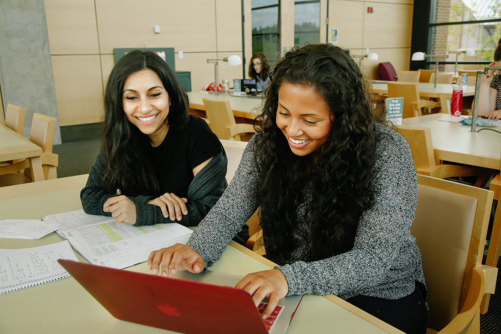 Two students working together and looking at a laptop.
