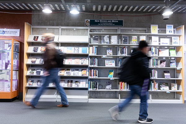 two students walking past each other in front of books