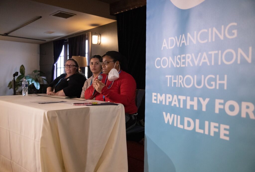 three people sitting at a table next to "Advancing conservation through empathy for wildlife conference" sign