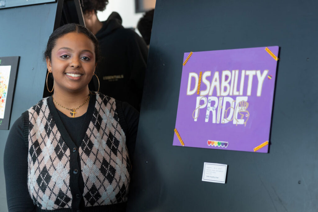 A person next to a piece of art that says "Disability Pride."