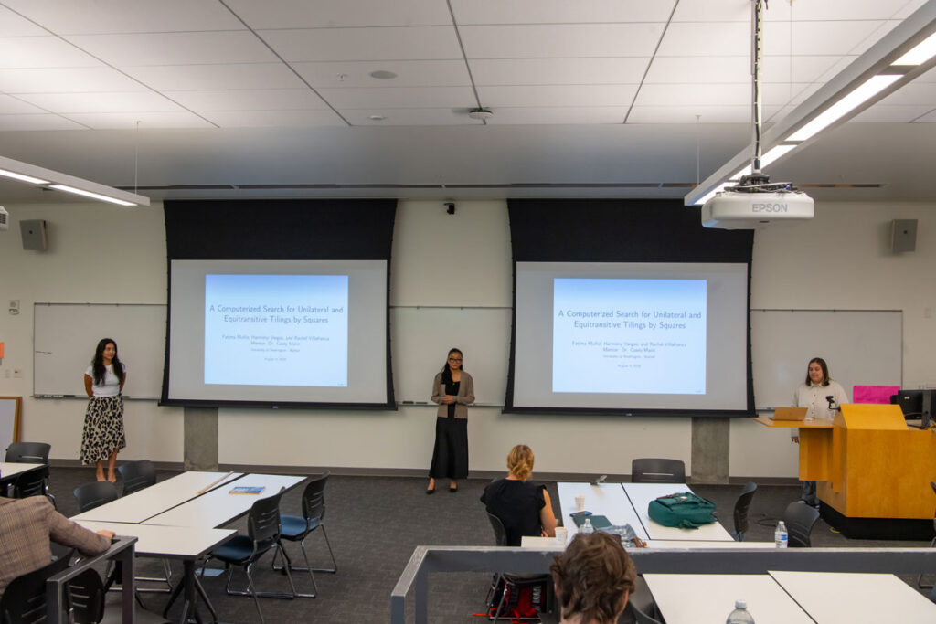 Three people present at the front of a classroom.