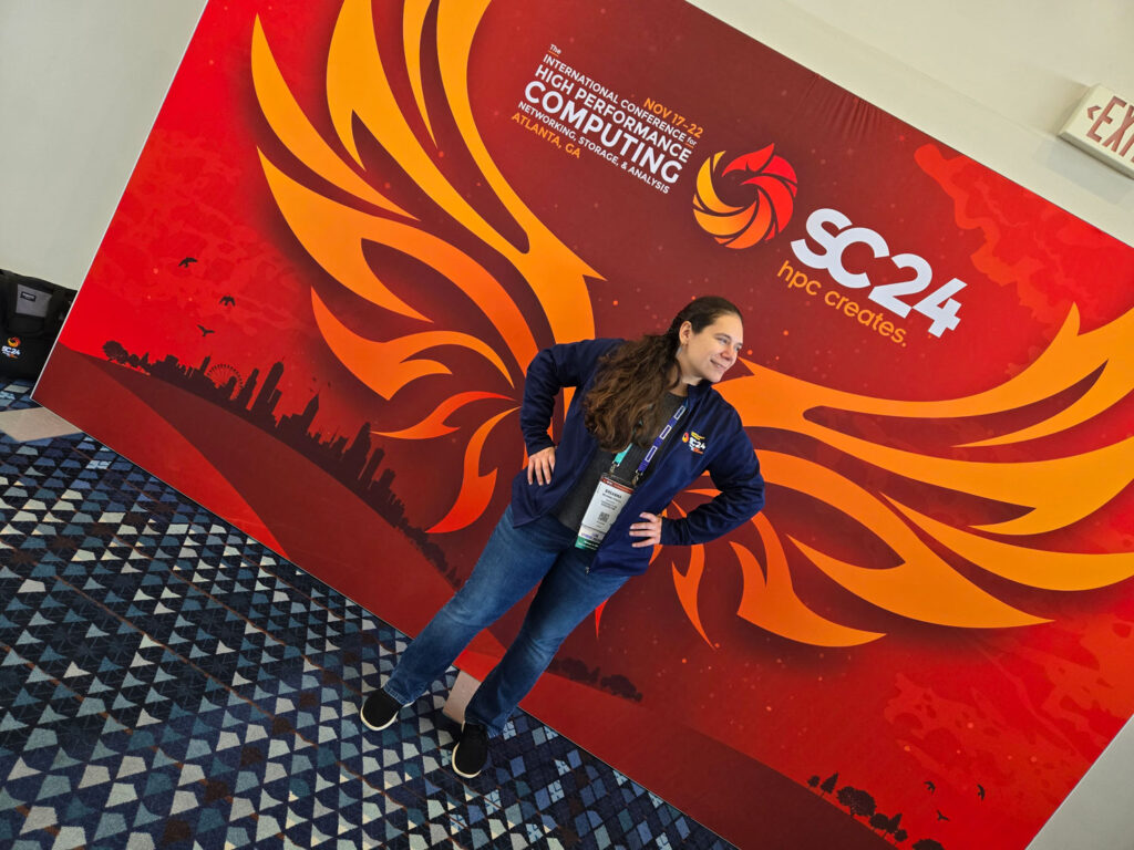 A person posing in front of a poster for a SC24 conference.