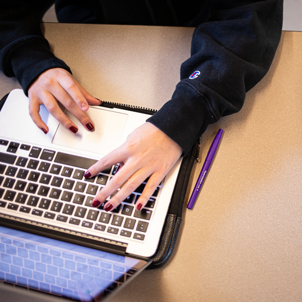 Woman with black sleeves typing on silver laptop.