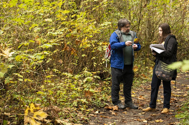 Warren Gold talks with student in forest.