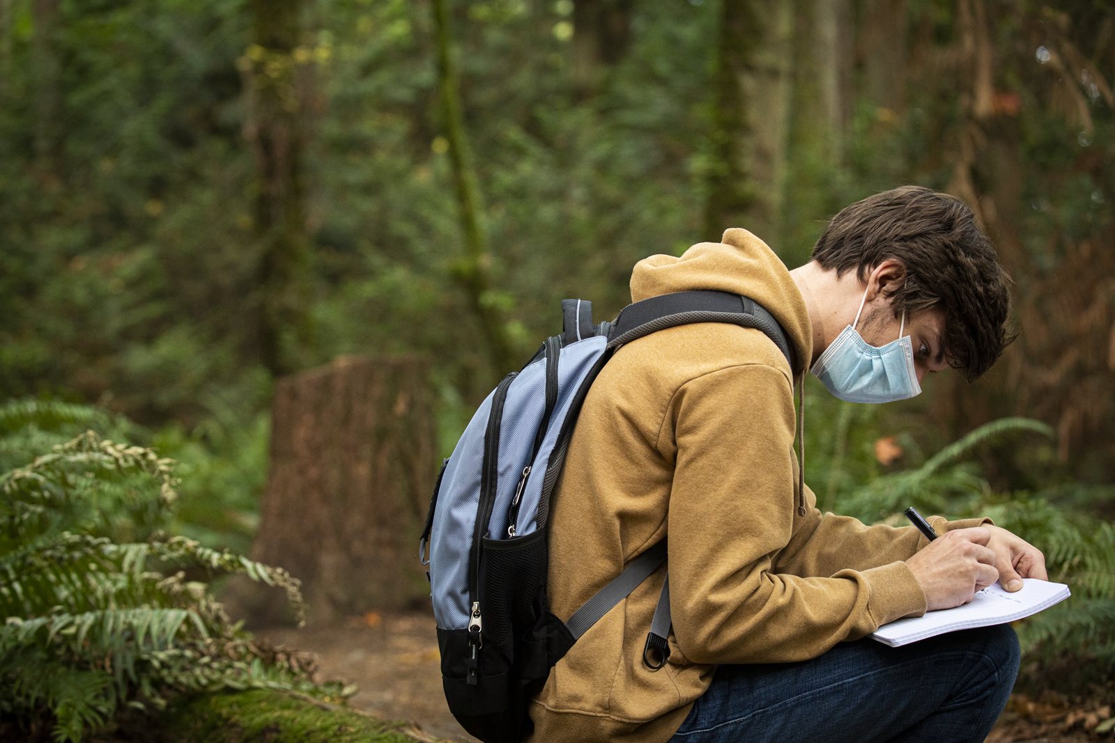 masked student sitting in the forest writing