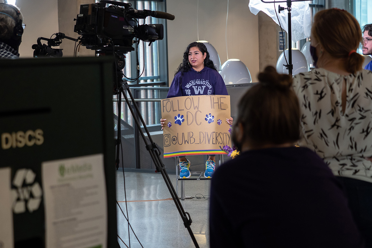 Diana holding a sign reading follow the Diversity Center  at UWB_Diversity while being filmed
